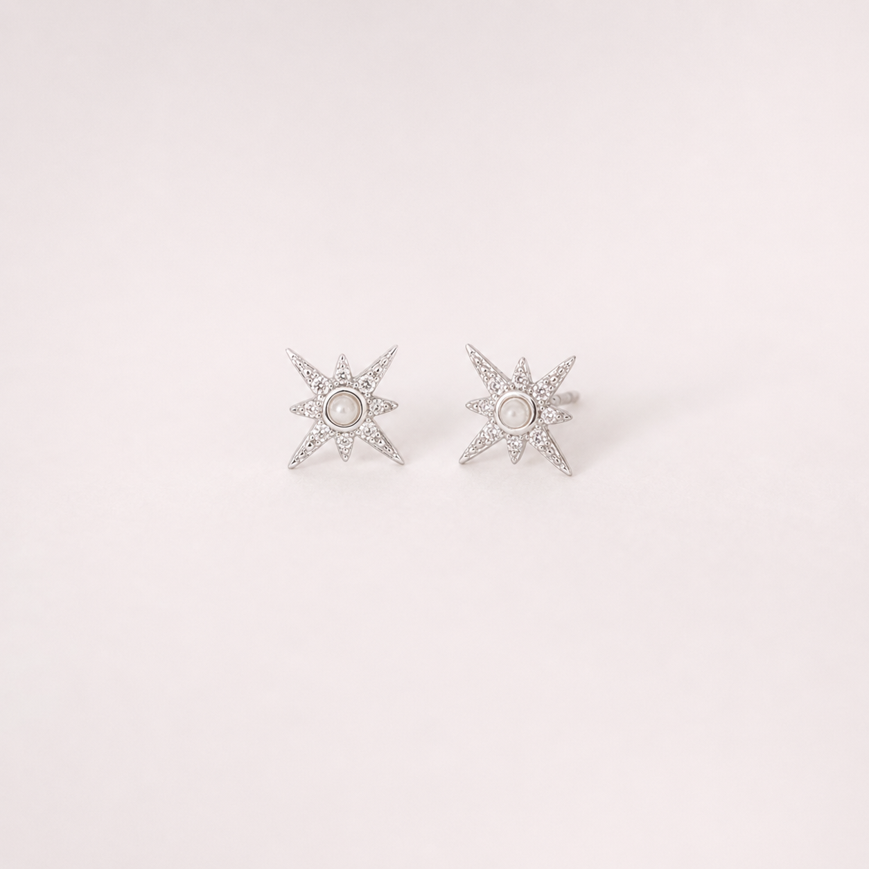 Star-shaped silver earrings with clear stones on a light pink background